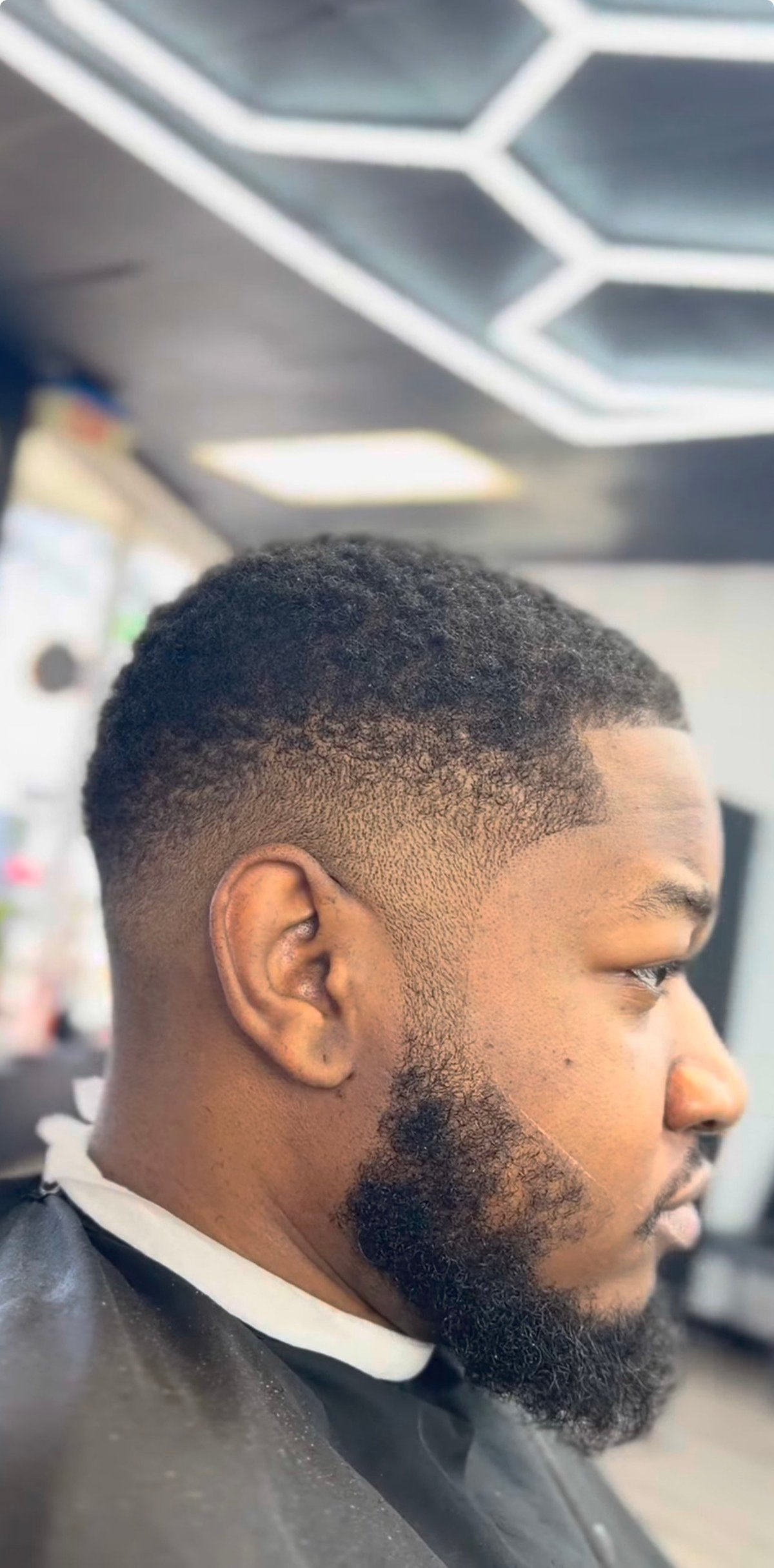 Fresh mid-fade with styled beard, hexagonal LED ceiling lights in the background
